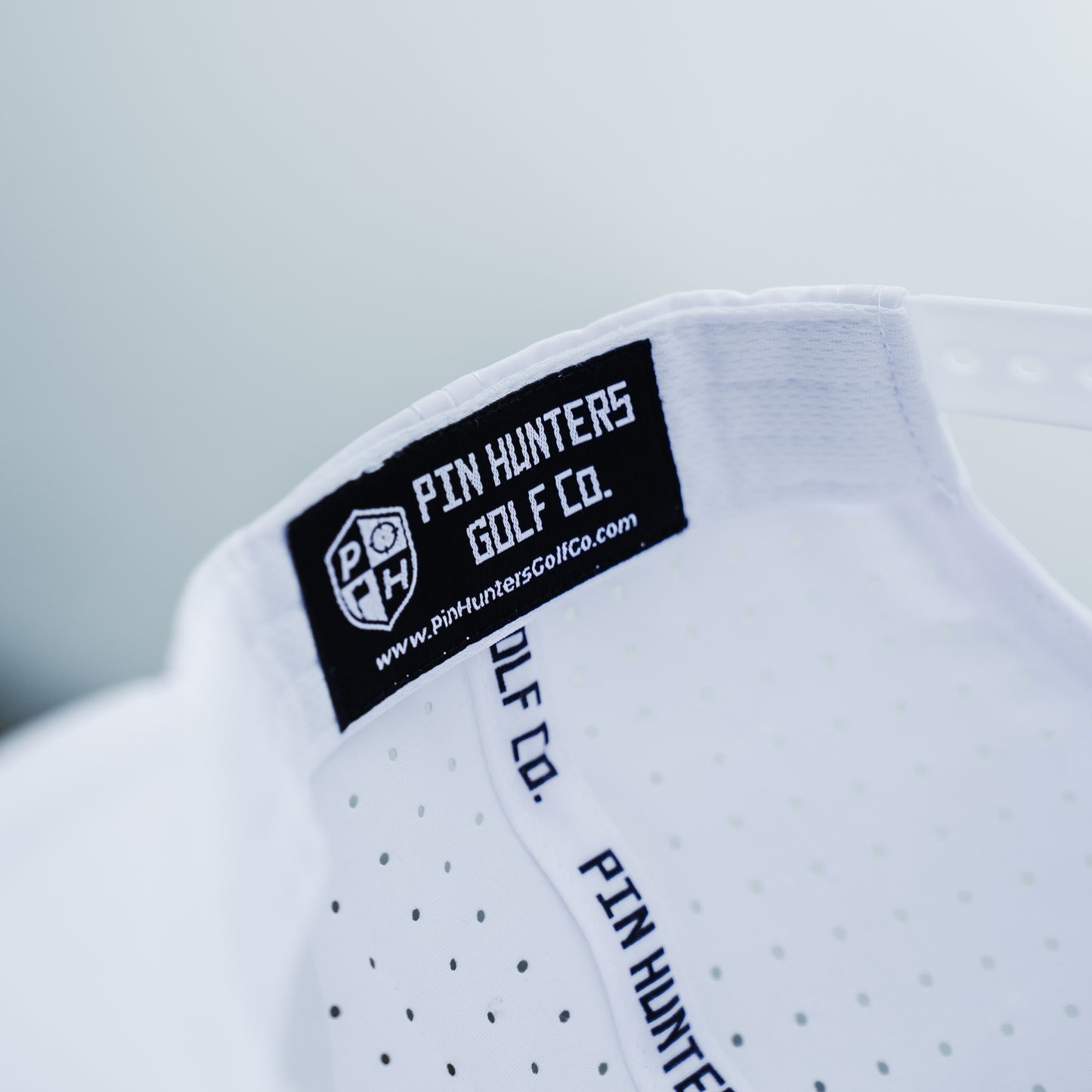 Close-up of white performance hat interior branding with black woven label, printed seam tape, and perforated fabric.