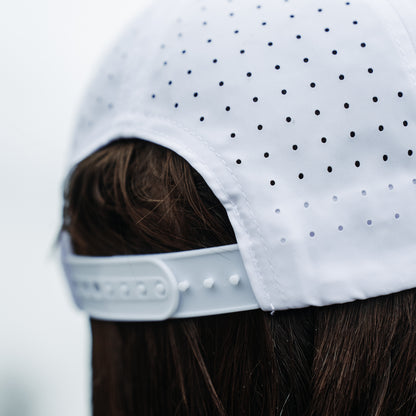 White performance hat back close-up with perforated panels, adjustable snapback closure, curved opening, and clean white stitching.