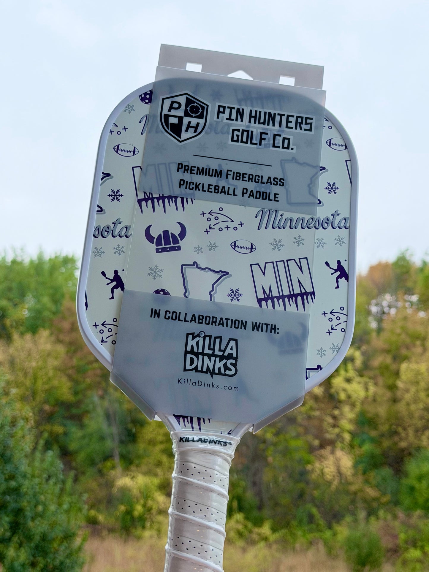 White Minnesota pickleball paddle in retail packaging with purple MIN graphics, Viking helmet icons, football details, snowflakes, and Killa Dinks collaboration label.