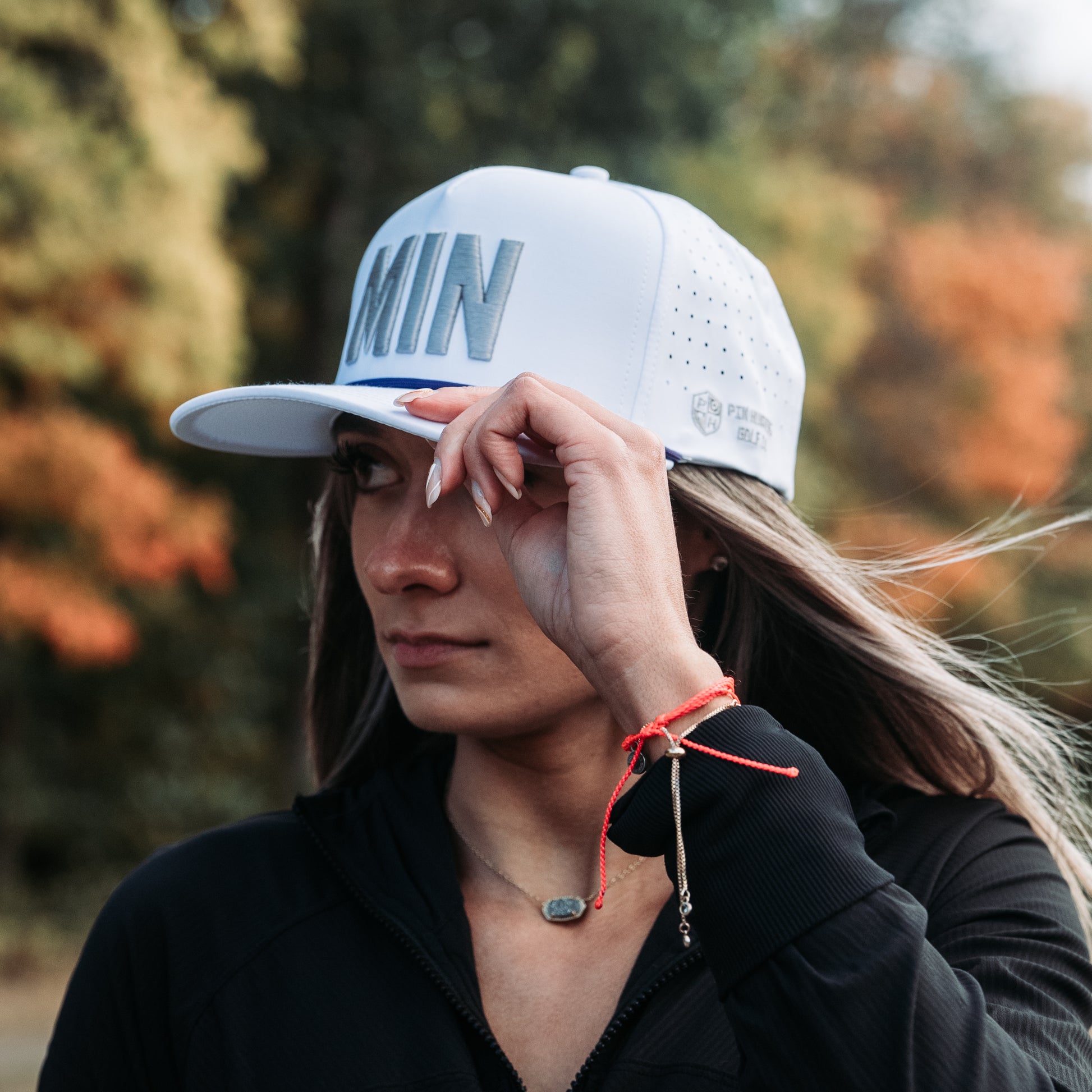 White tonal MIN performance golf hat on model with raised white embroidery, matching rope detail, side logo, and perforated panels.
