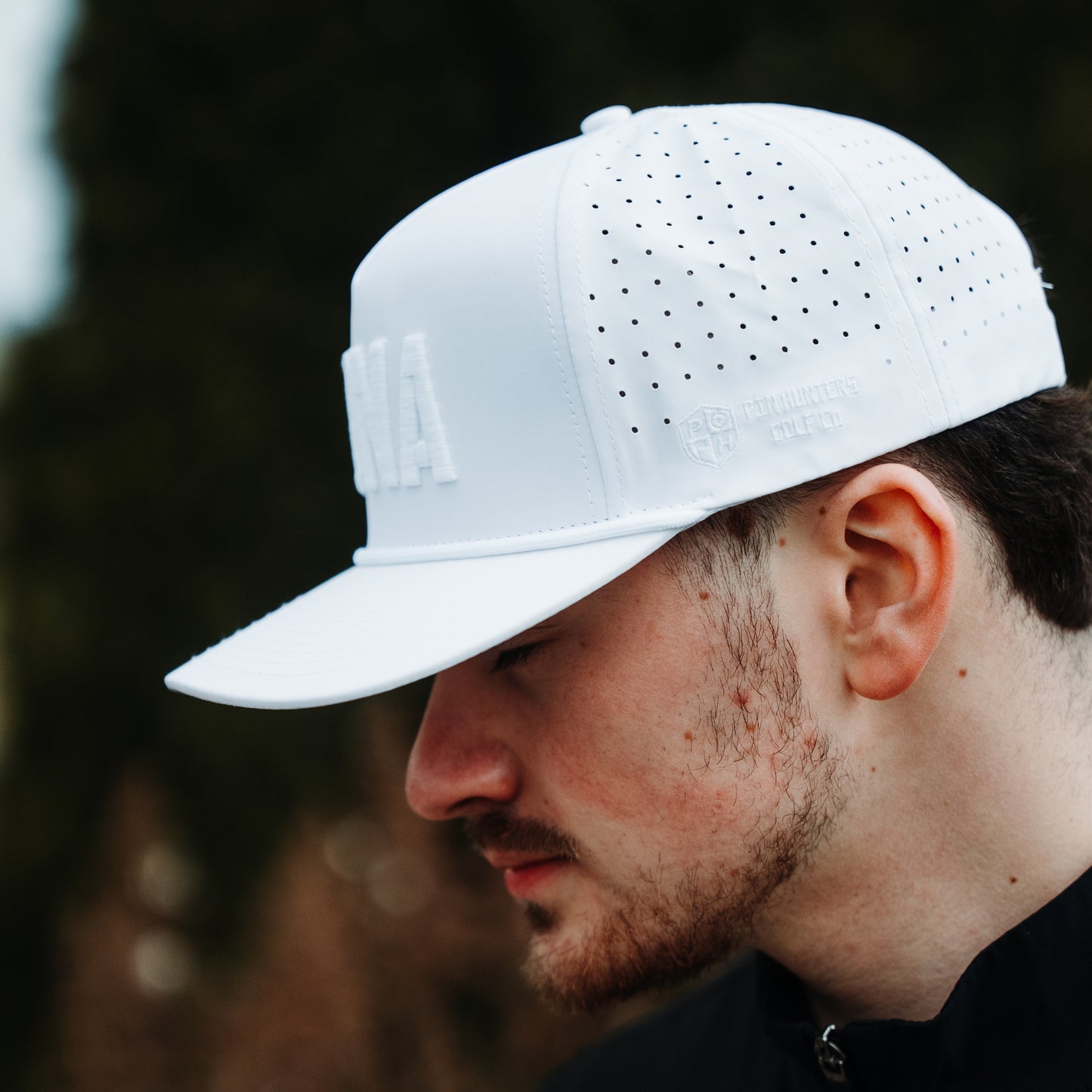 White USA tonal performance golf hat on model with white embroidery, matching rope detail, perforated side panels, and side logo.