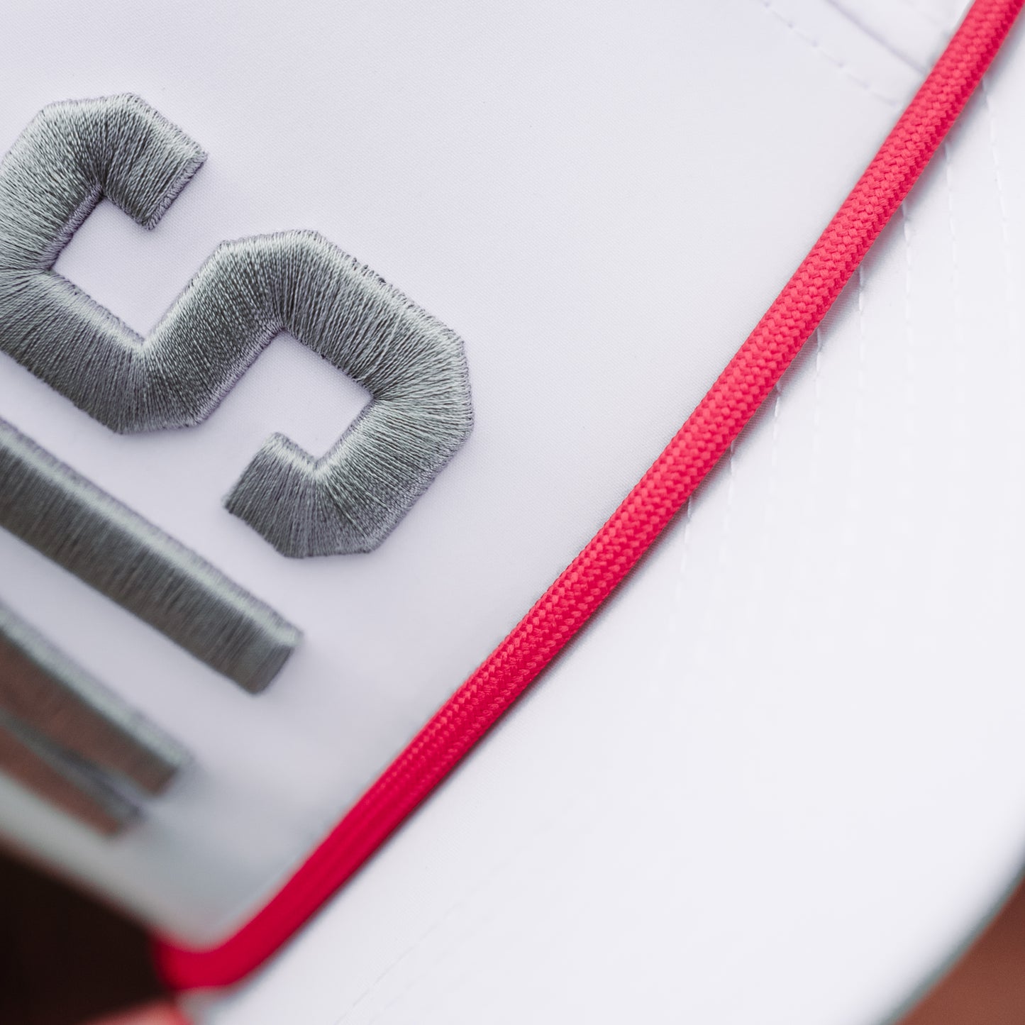 White WIS performance golf hat close-up with gray raised embroidery, red rope detail, and clean white performance fabric.