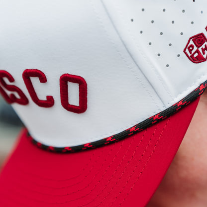 White Wisco performance golf hat close-up with red raised embroidery, red brim, black and red rope detail, and side logo.