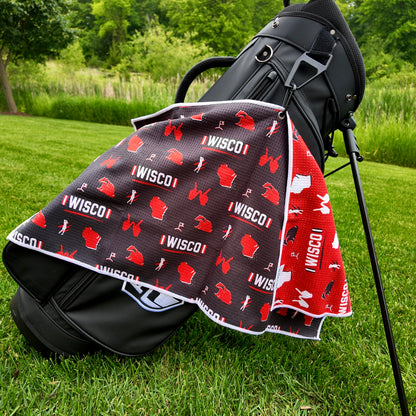 Wisconsin Badgers black golf towel hanging on a black golf bag with I WISCO text, red Wisconsin outlines, badger graphics, golfers, golf flags, and red reverse side.