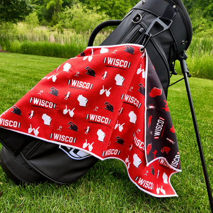 Wisconsin Badgers red golf towel hanging on a black golf bag with I WISCO text, white Wisconsin outlines, badger graphics, golfers, golf flags, and black reverse side.