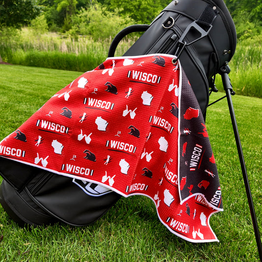 Wisconsin Badgers red golf towel hanging on a black golf bag with I WISCO text, white Wisconsin outlines, badger graphics, golfers, golf flags, and black reverse side.