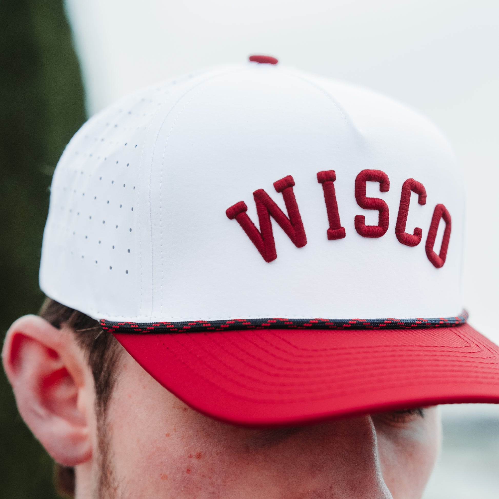 Wisconsin Badgers performance hat close-up with white crown, red WISCO raised embroidery, red brim, black and red rope detail, and perforated side panels.
